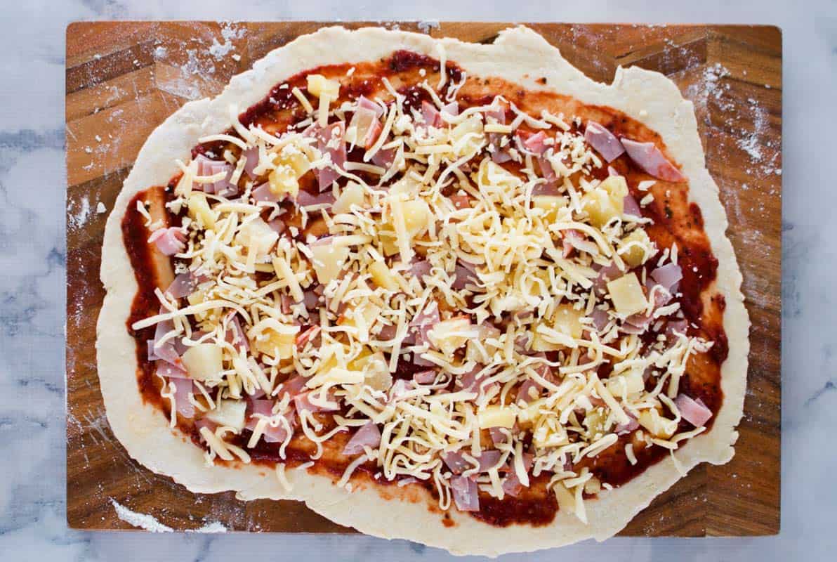 Pizza sauce, ham, pineapple and cheese on top of dough.