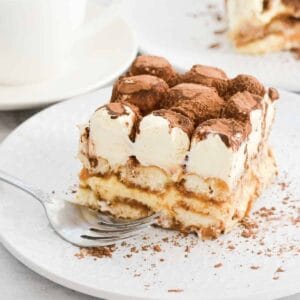 A piece of tiramisu on a plate with cocoa and whipped cream on top.