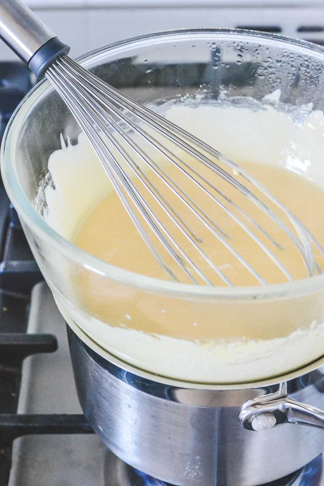 A whisk in a glass bowl over a saucepan of simmering water.