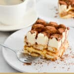 A piece of tiramisu on a plate with cocoa and whipped cream on top.