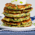 Six vegetable fritters in a stack with sour cream on top.
