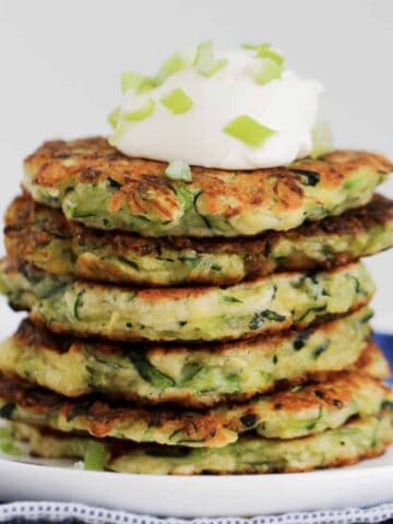 Six vegetable fritters in a stack with sour cream on top.