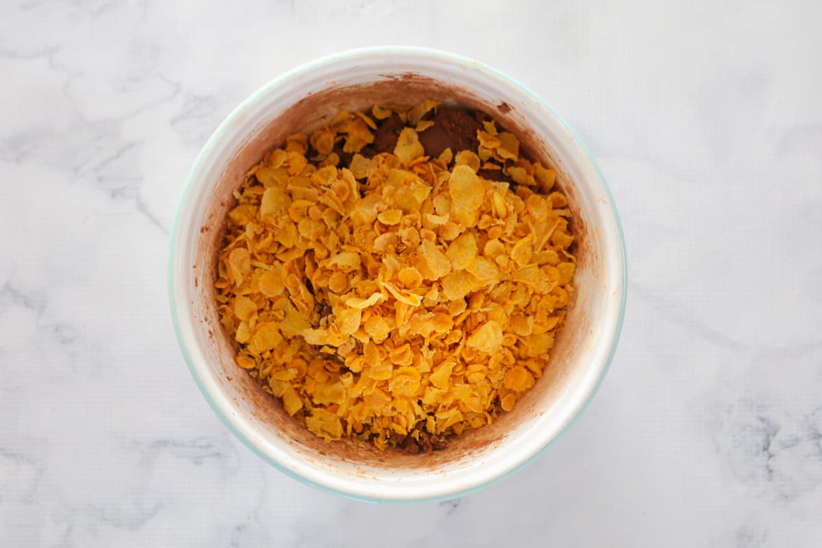 Cornflakes in a mixing bowl with chocolate biscuit mixture underneath.