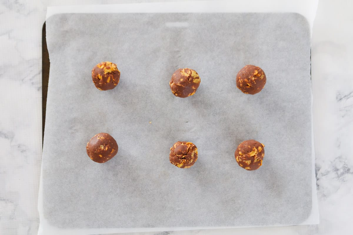 Balls of chocolate and cornflake biscuit dough on a baking tray.