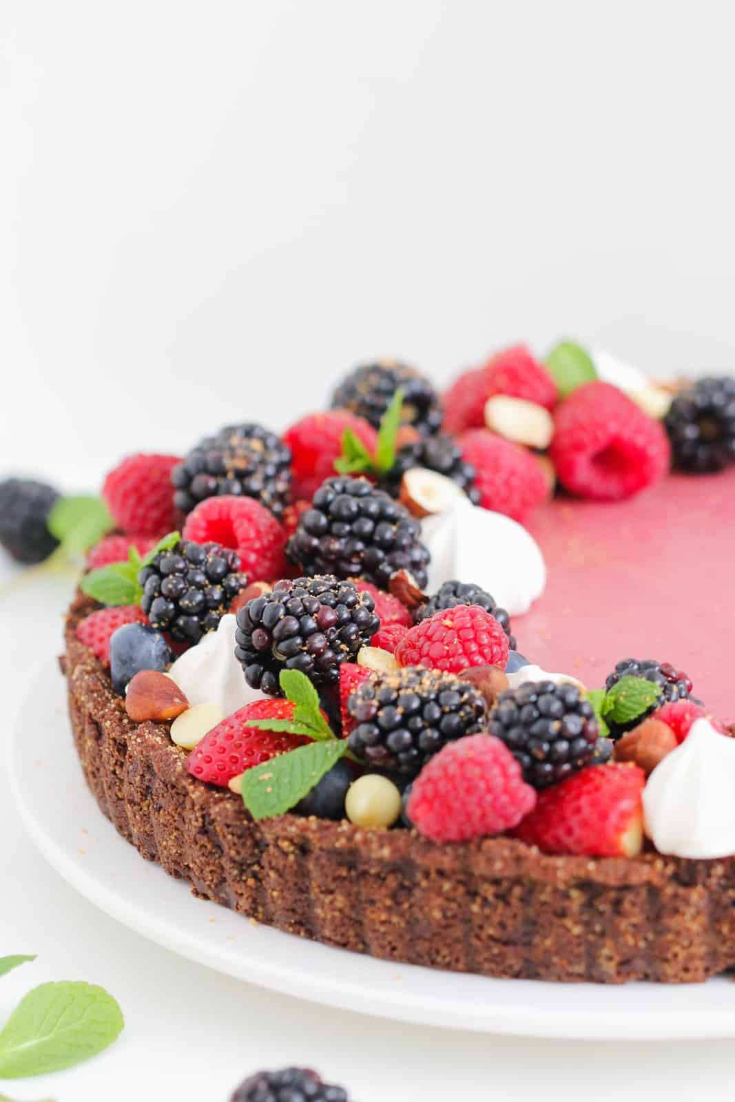 A berry tart with a chocolate base covered with fresh berries and mint leaves and meringues.