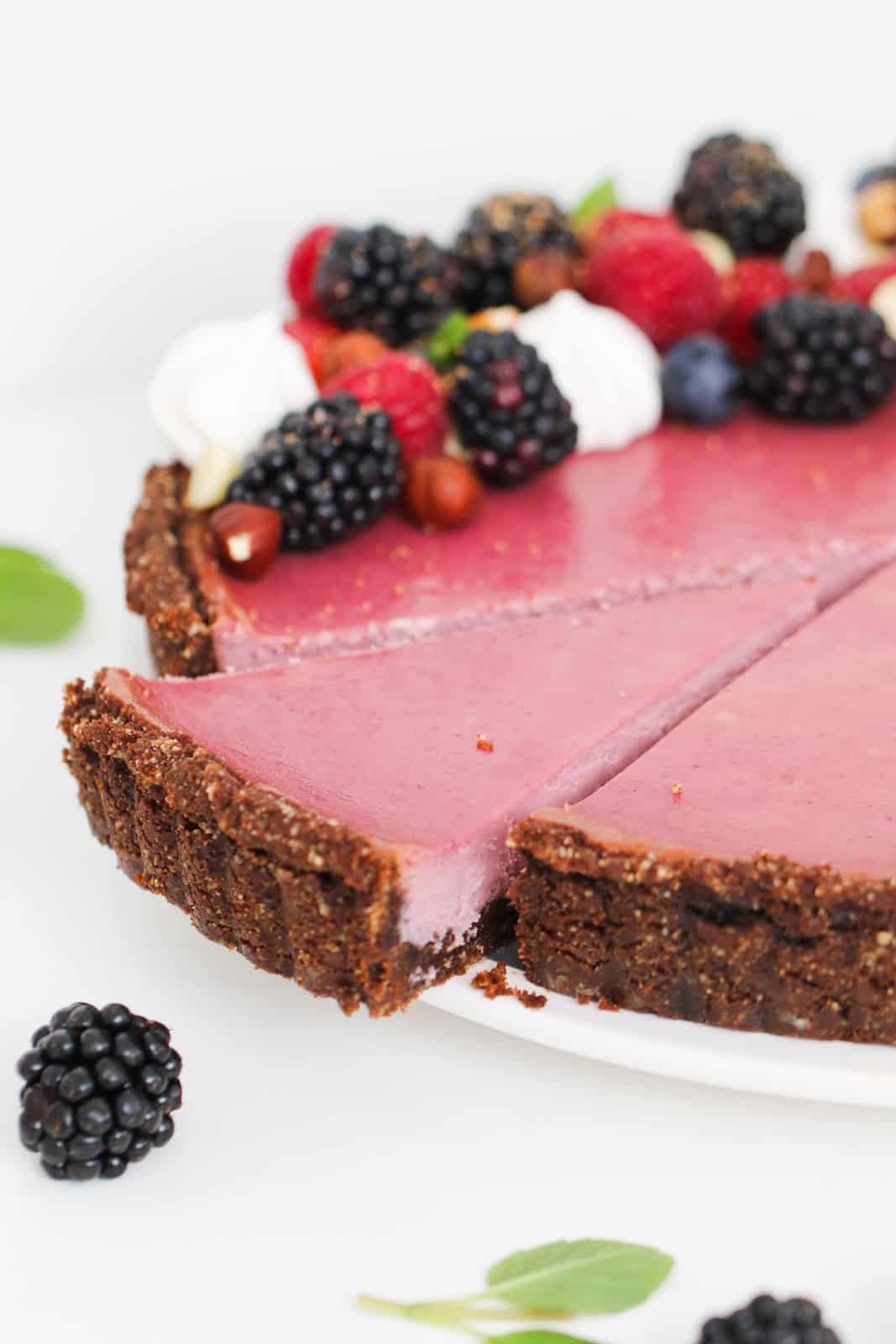 A slice of berry cheesecake being removed from a chocolate berry tart with fresh berries on top.