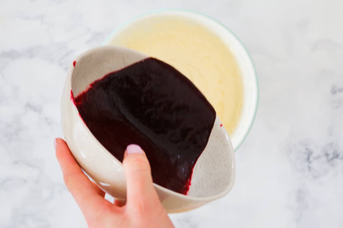 Blackberry puree being poured onto a bowl of cheesecake mixture.