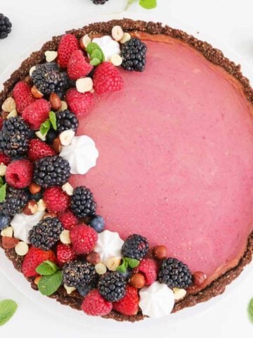 A pink cheesecake covered with berries, mint leaves and meringues with a chocolate crust.