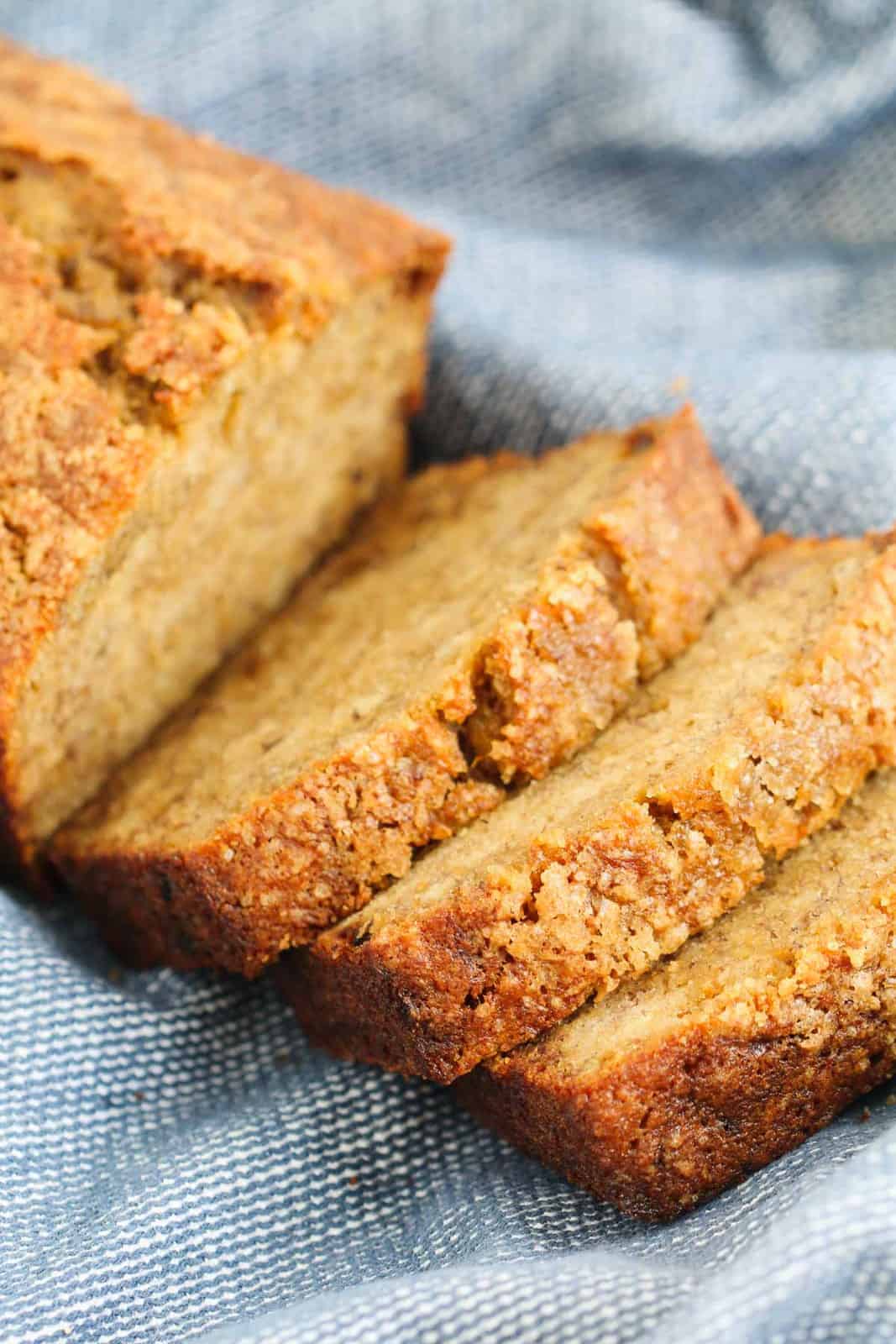Slices of banana loaf with a crunchy top, resting on a blue tea towel.