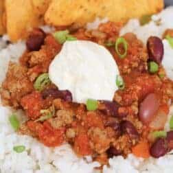 A bowl of rice rice, slow cooker chilli con carne, sour cream and corn chips.