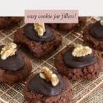 A batch of chocolate cookies, with chocolate icing and a piece of walnut on top, freshly baked.
