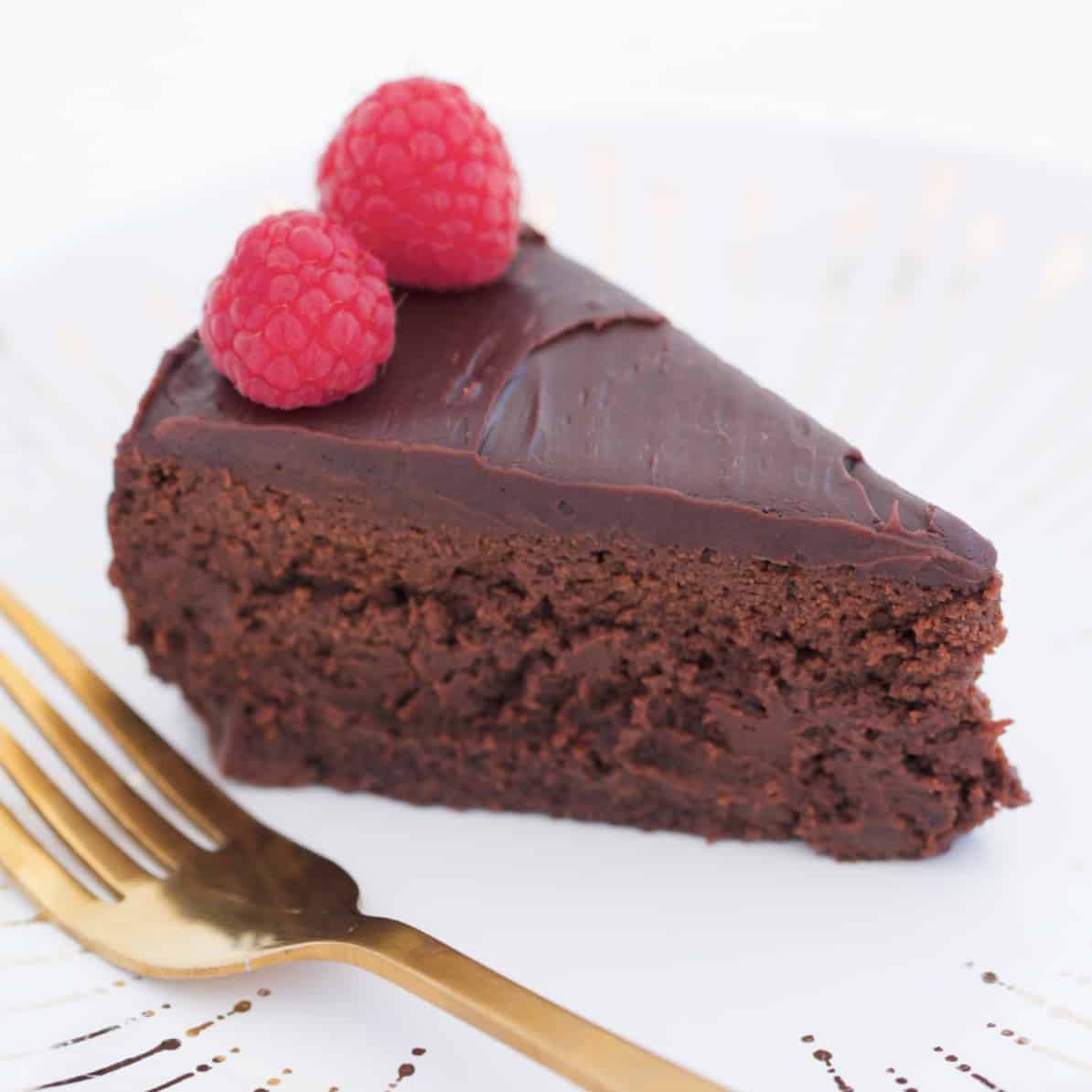 A slice of rich chocolate cake with chocolate ganache and raspberries.