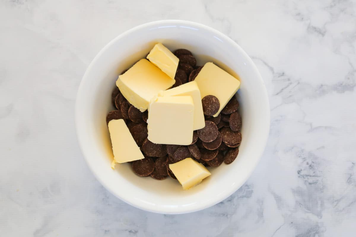 Dark chocolate melts and chunks of butter in a white mixing bowl.