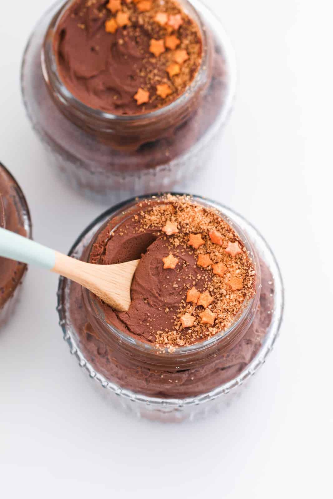 A spoon being dipped into a glass jar of chocolate mousse with gold decorations.