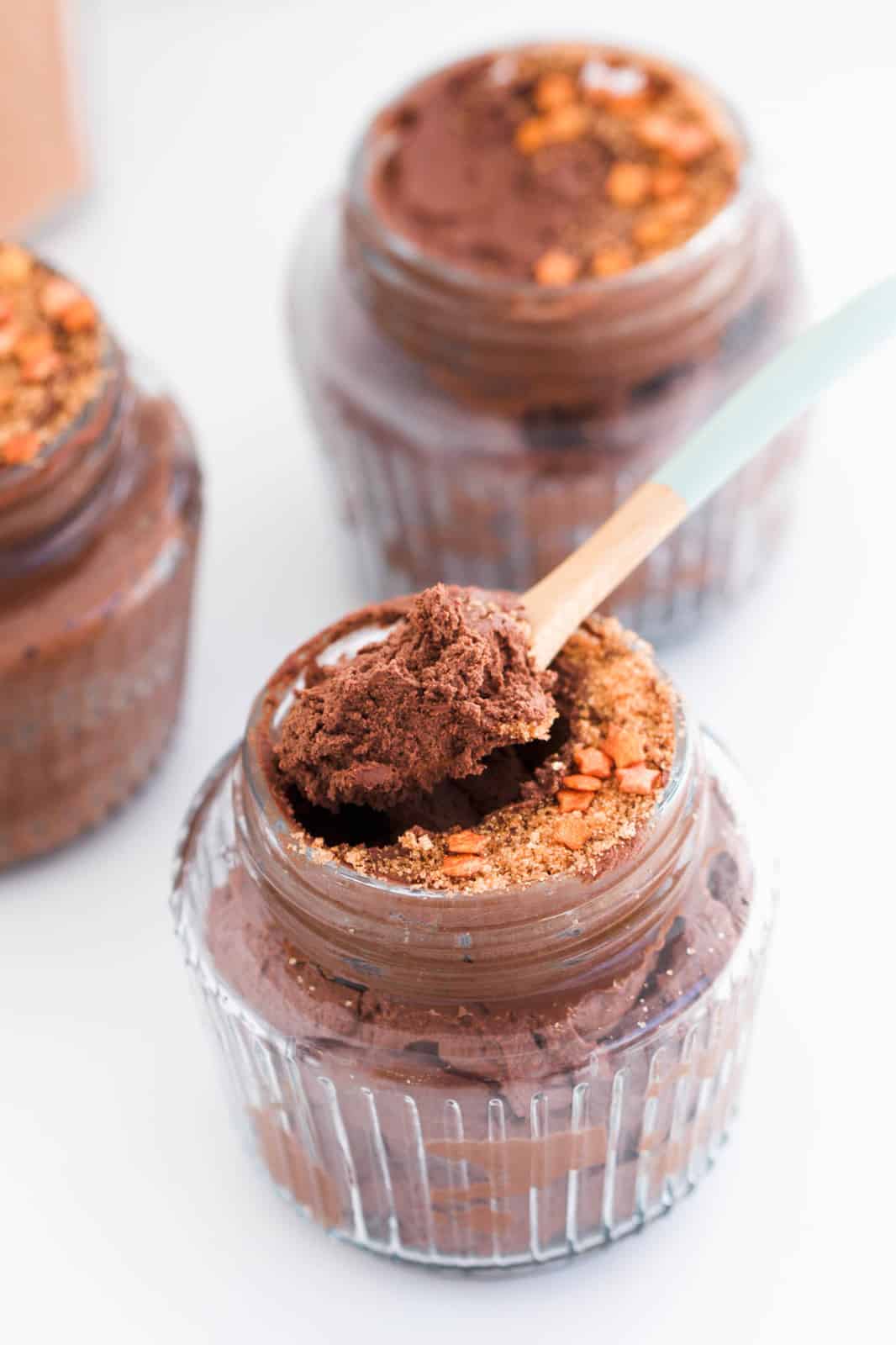 A wooden spoon lifting a chocolate mousse dessert out of a glass jar.