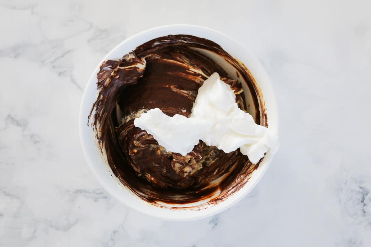 Whipped egg whites on top of chocolate mixture in a bowl.