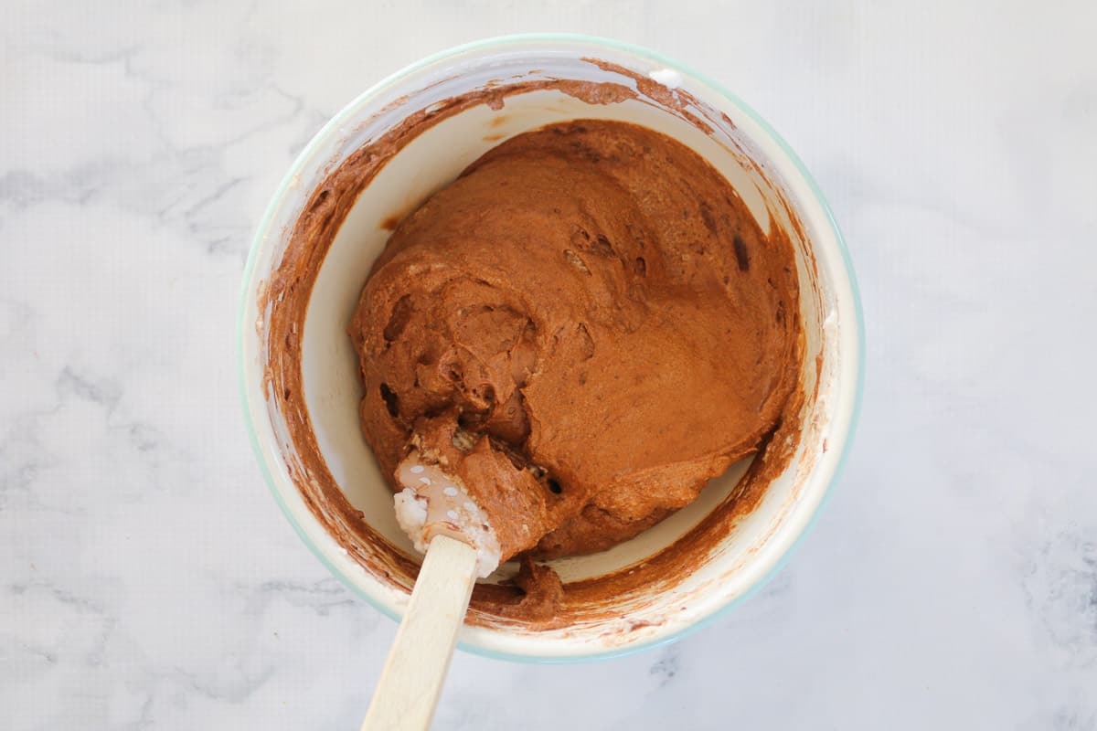A spatula folding through a chocolate mousse mixture in a bowl.