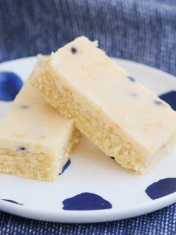 Two pieces of baked slice topped a creamy passionfruit topping on a white and blue plate.