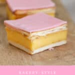 Pieces of custard slice with pastry and pink icing glaze on a wooden board.