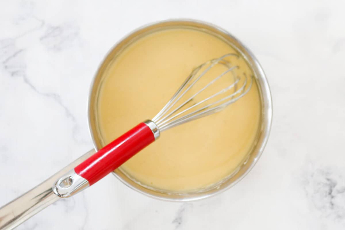 A whisk sitting in a saucepan of custard on a marble bench