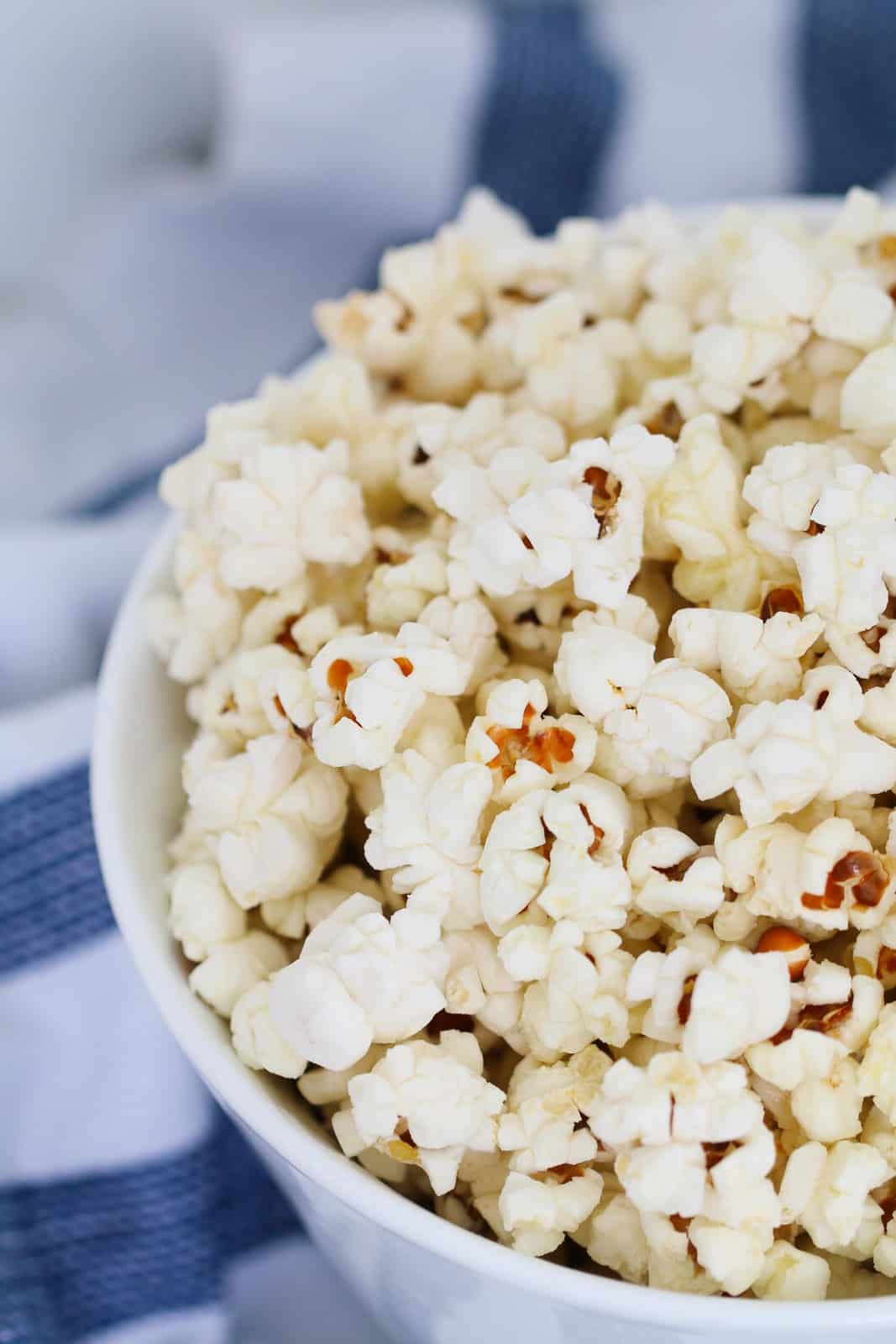 An overhead shot of a white bowl of popcorn on a white and blue tea towel.