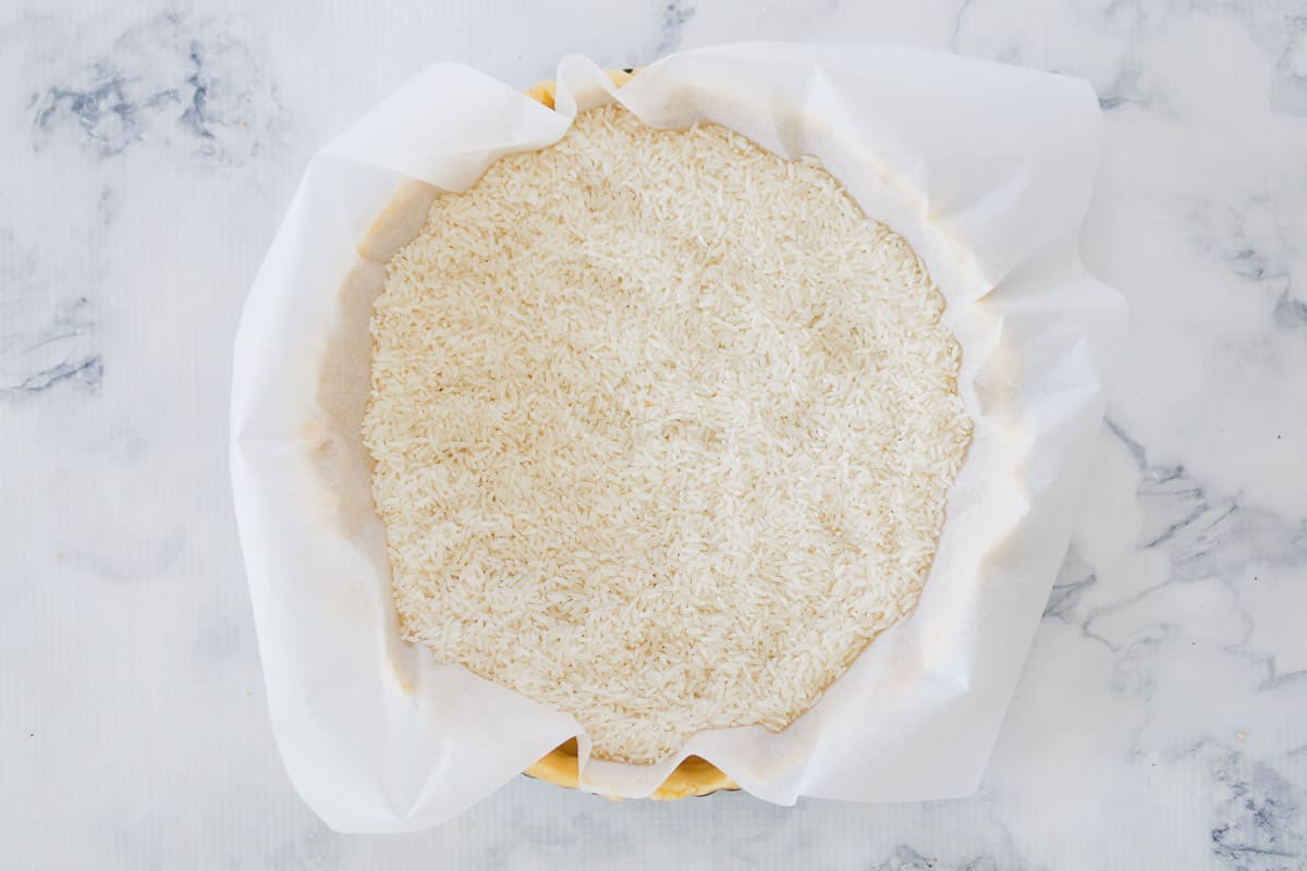 Rice on top of baking paper in a tart tin with pastry before blind baking.