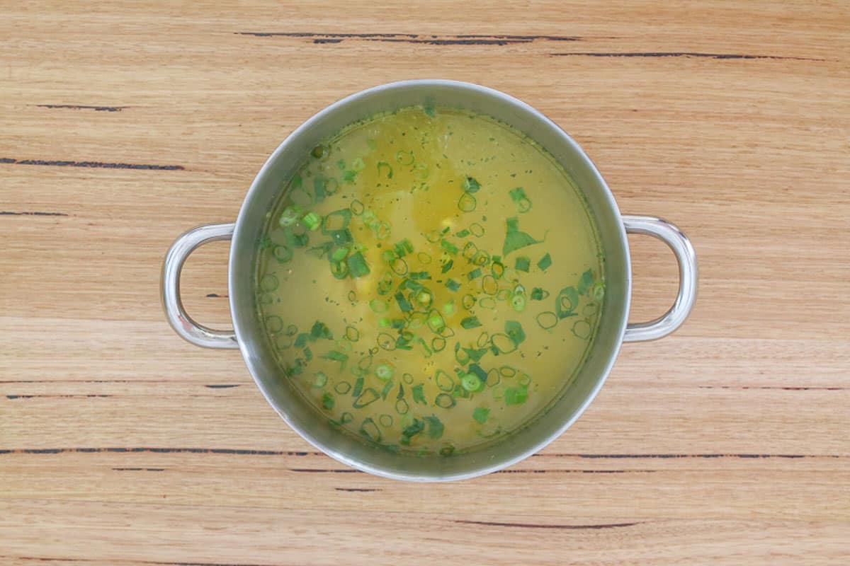 A pot of chicken stock, corn and spring onions.