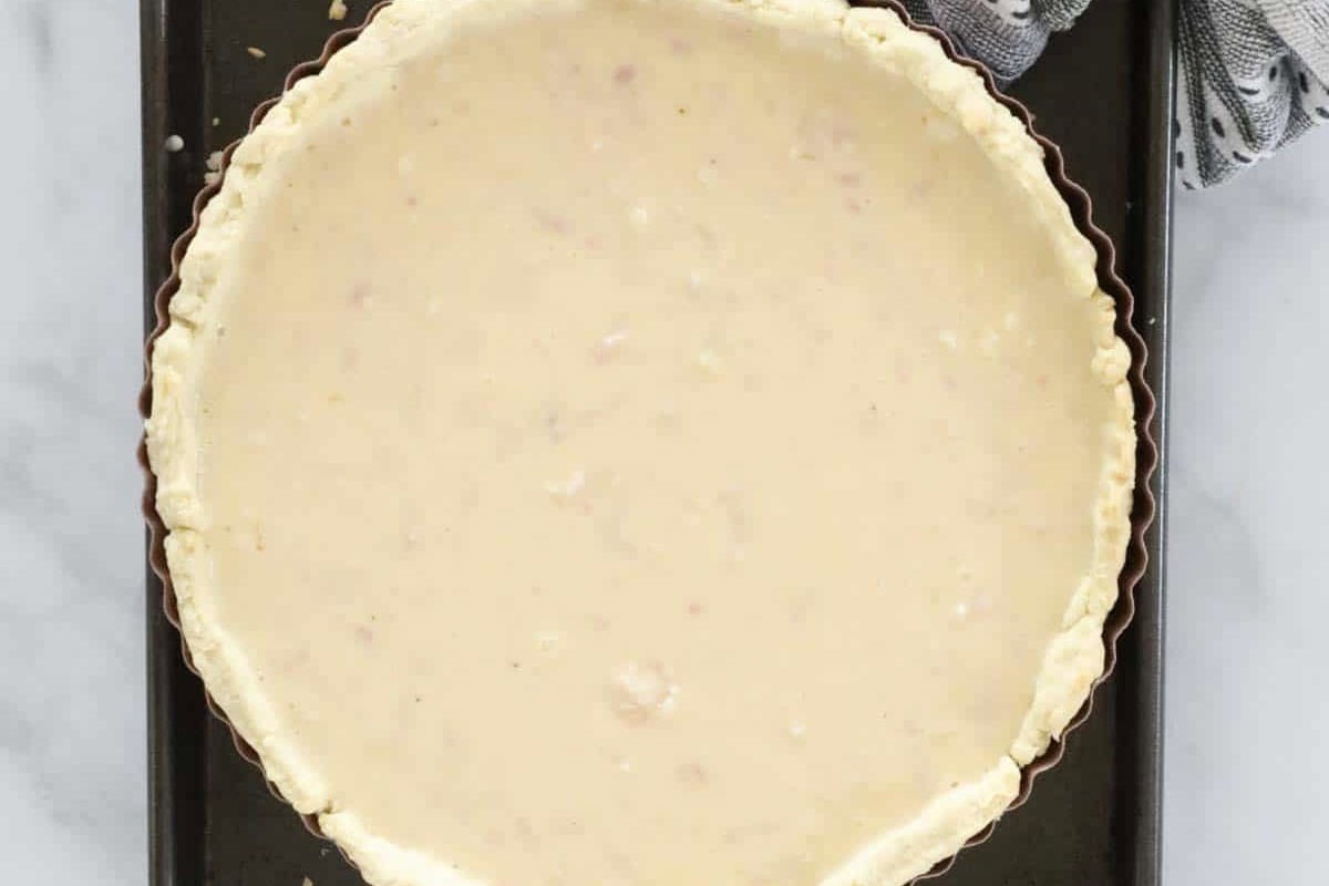 Quiche filling in an pastry shell on a black tray.