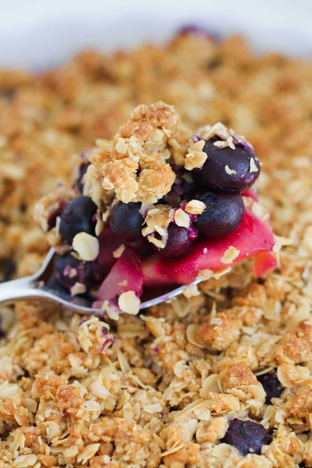 A spoon full of apple and blueberries being lifted from a baked crumble.