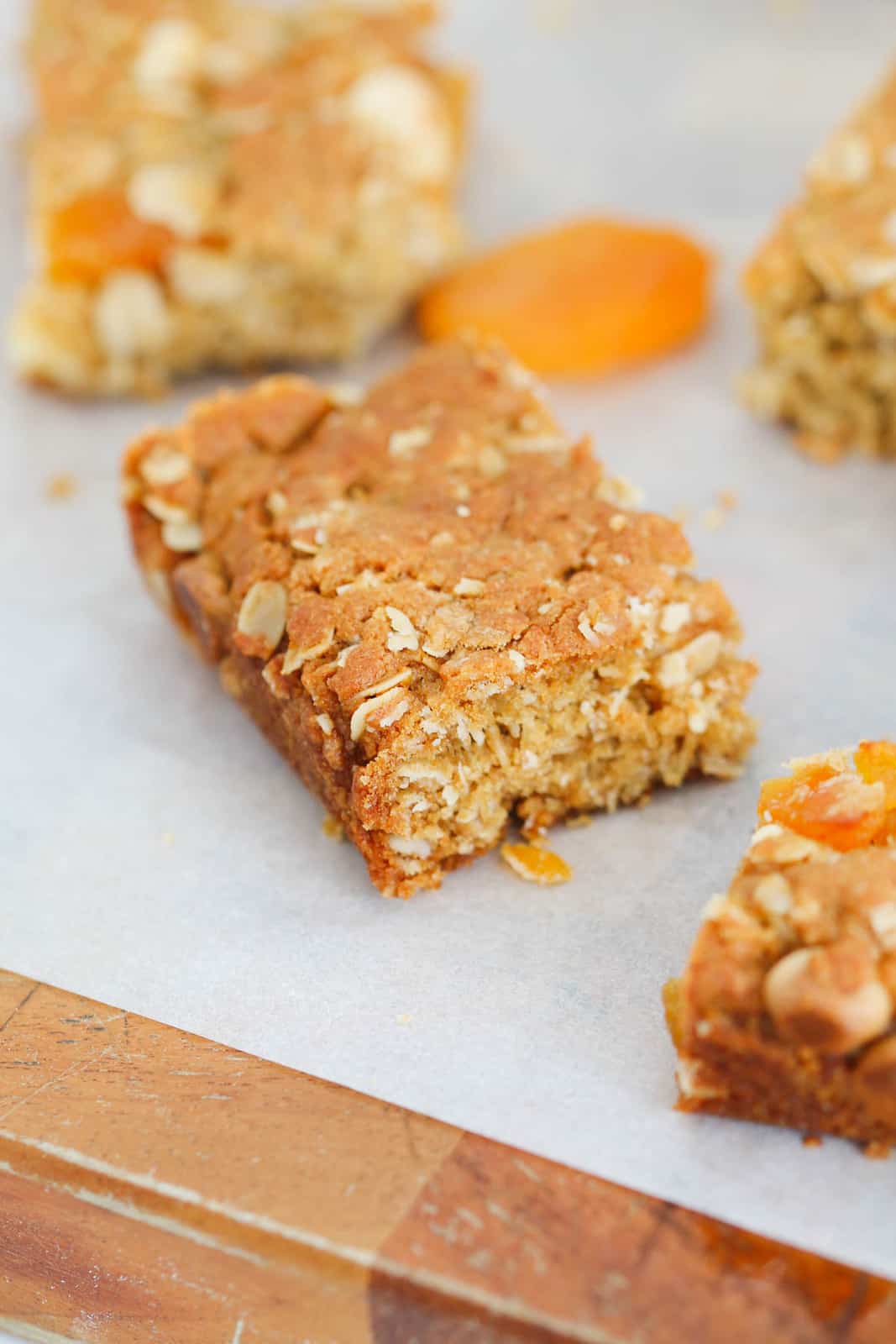 An square of apricot oat slice on a piece of paper surrounded by other slices and dried apricots