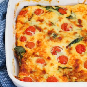 A white baking dish filled with an egg mixture, tomatoes, spinach and cheese.