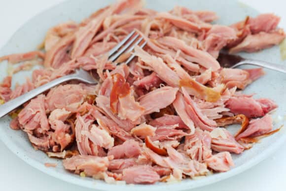 A ham hock being shredded with two forks.