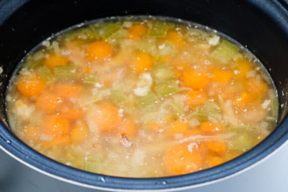 A slow cooker filled with simmering vegetable broth, ham hock and vegetables.