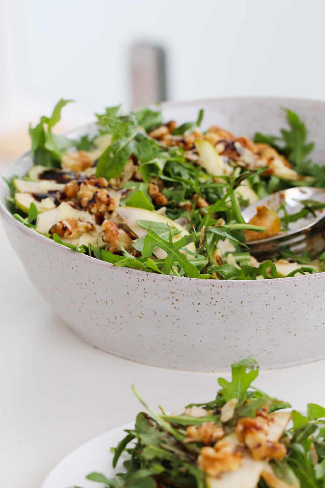A bowl of fresh salad with walnuts, pear, rocket, parmesan and a balsamic glaze.