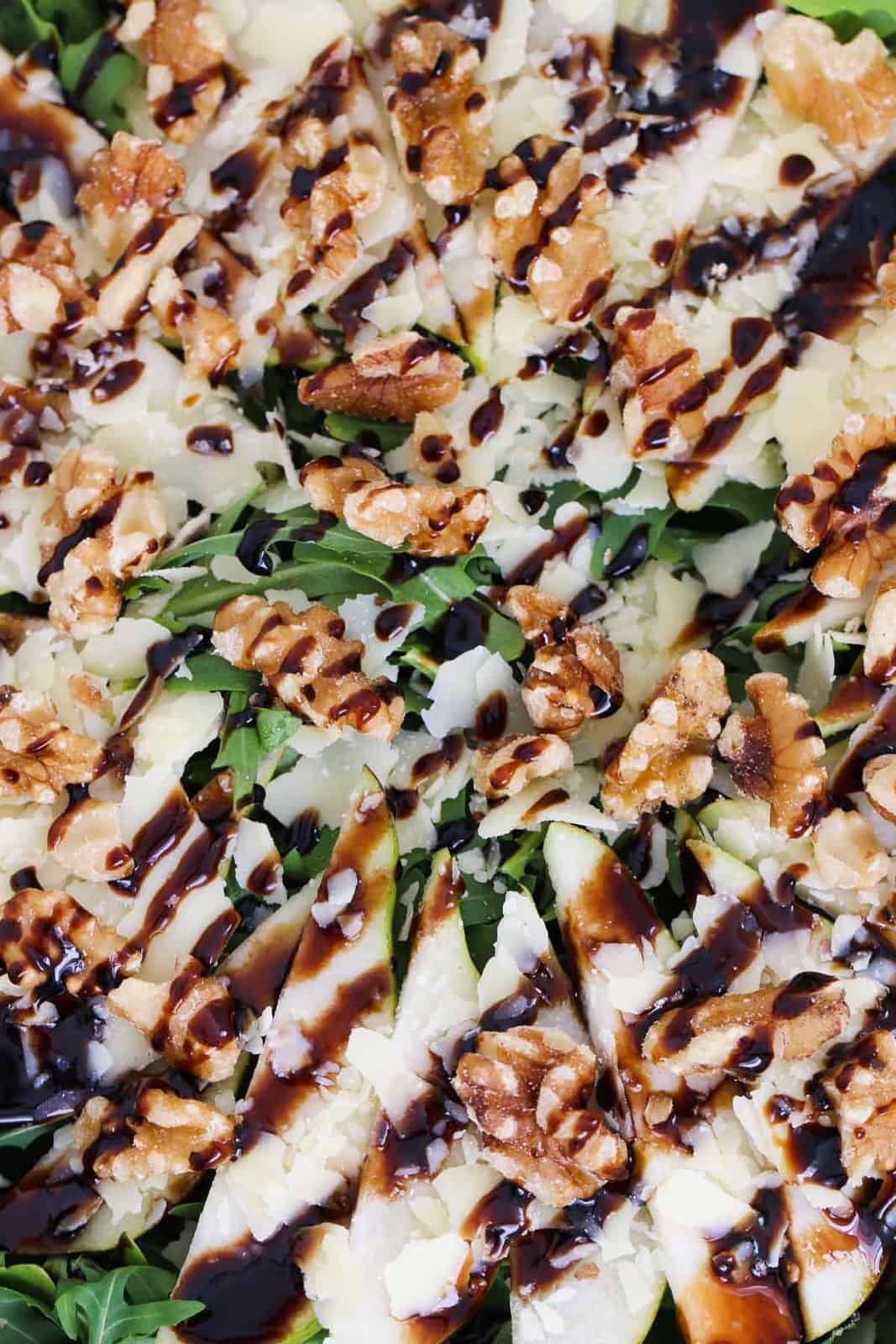 A close up overhead shot of balsamic glaze over a pear, rocket and parmesan salad sprinkled with walnuts.