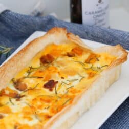 Roast Pumpkin, Caramelized Onion & Feta Tart on a serving dish with a jar of caramelized onions in the background