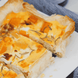A puff pastry tart sliced into pieces showing pumpkin, feta, caramelised onion and rosemary in an egg filling.