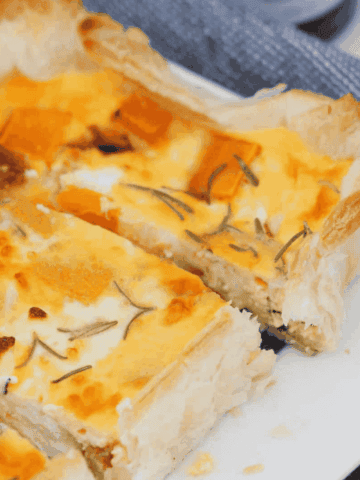 A puff pastry tart sliced into pieces showing pumpkin, feta, caramelised onion and rosemary in an egg filling.