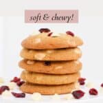 A stack of 5 cookies with wgite chocolate chips and dried cranberries sprinkled next to them.