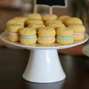 A white cake stand with yo yo biscuits that have pink and blue filling.