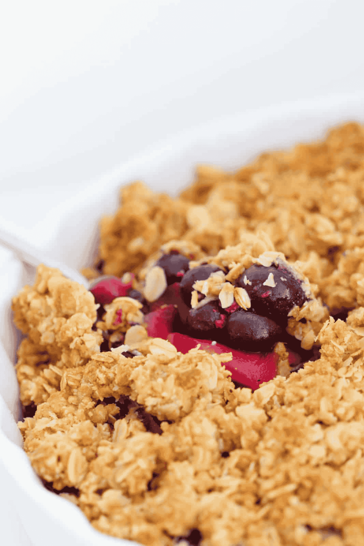A spoon lifting up apple and blueberry crumble with a golden crunchy oat topping.
