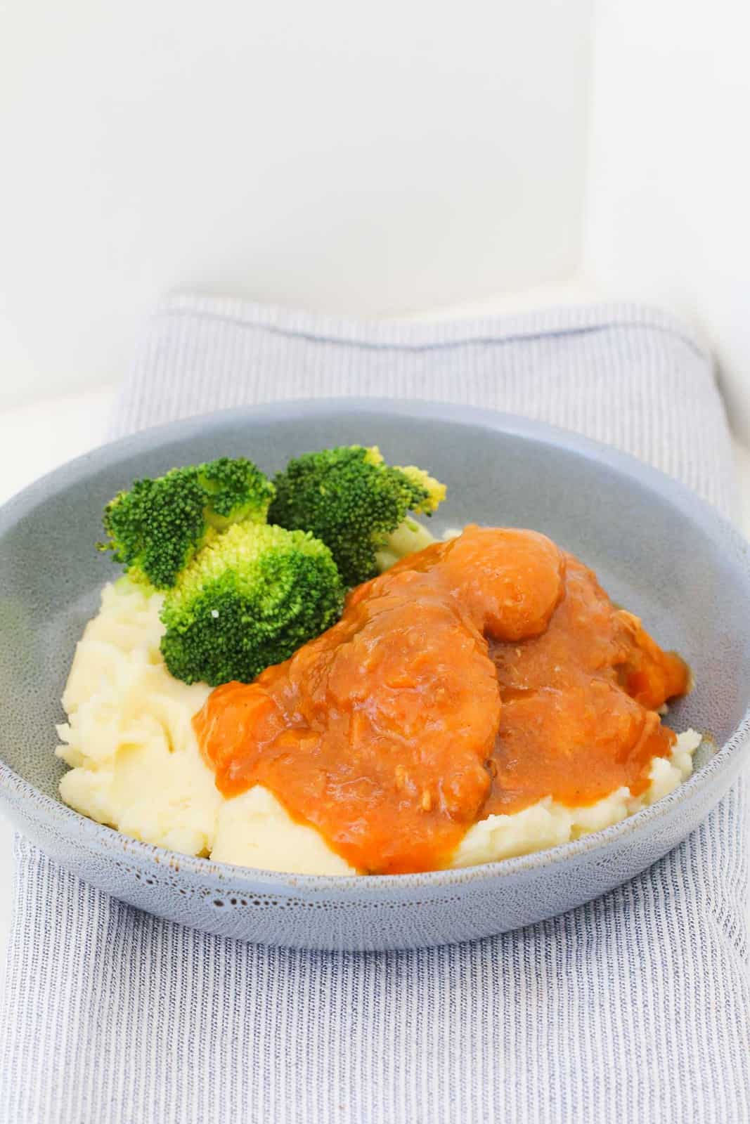 A bowl of apricot chicken with mashed potato and broccoli.