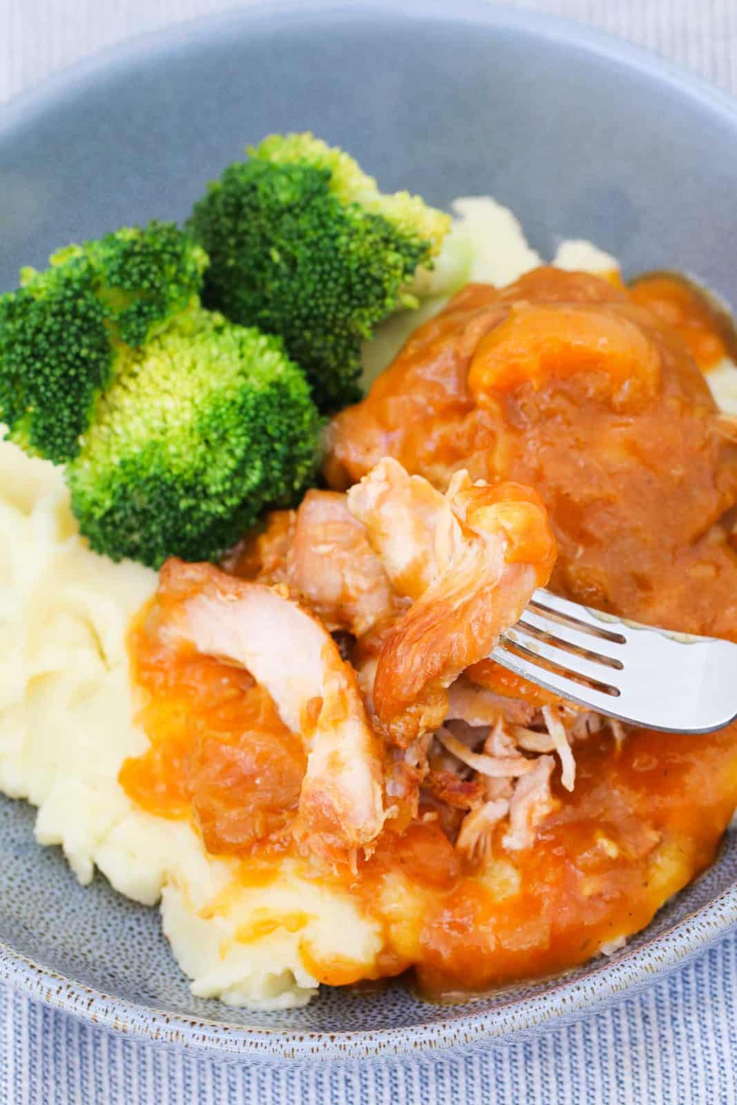 A fork with apricot chicken on a bed of mashed potato and greens.