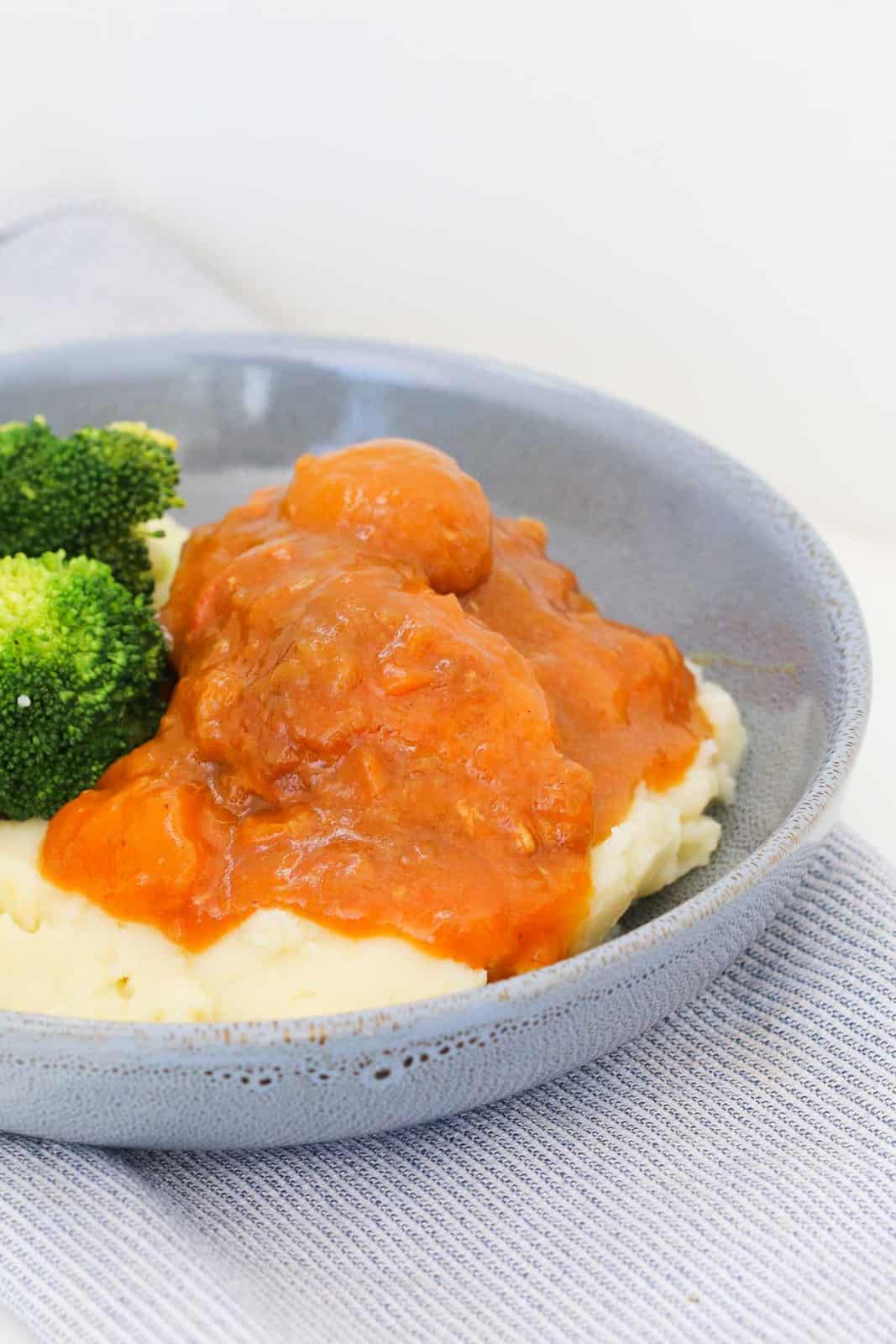A blue bowl filled with mashed potato, broccoli and chicken covered in apricot sauce.