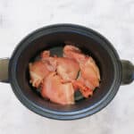 Chicken thighs in the base of a slow cooker.