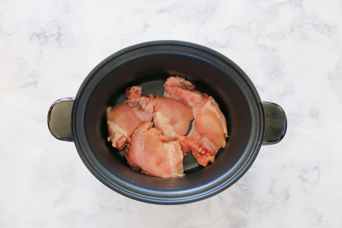 Chicken thigh fillets in the base of a slow cooker.