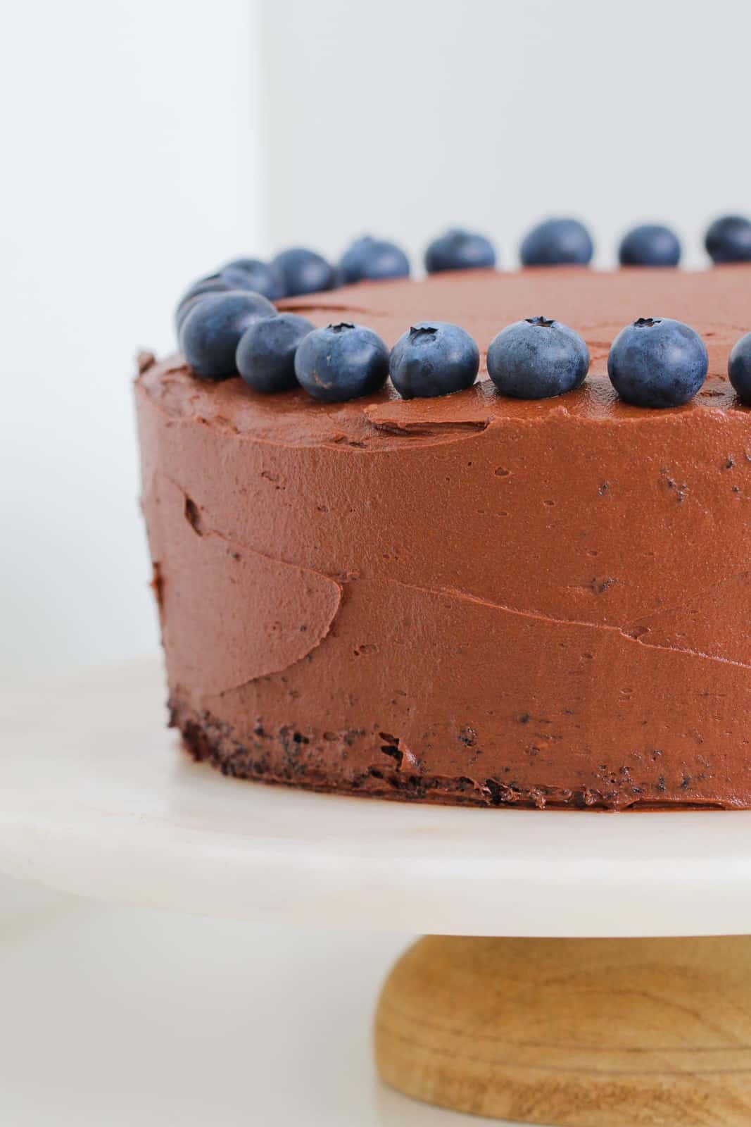 A chocolate frosted cake on a cake stand decorated with blueberries.