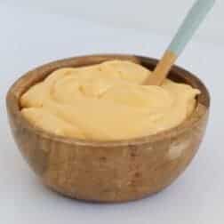 A spoon in a wooden bowl filled with creamy yellow lemon curd.