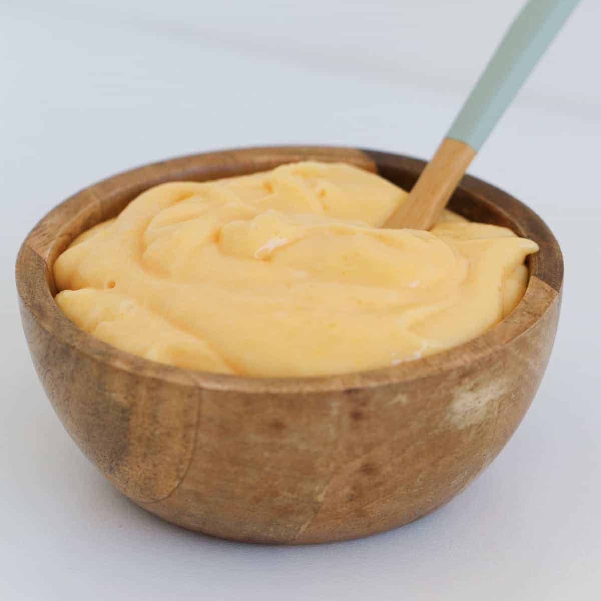 A spoon in a wooden bowl filled with creamy yellow lemon curd.