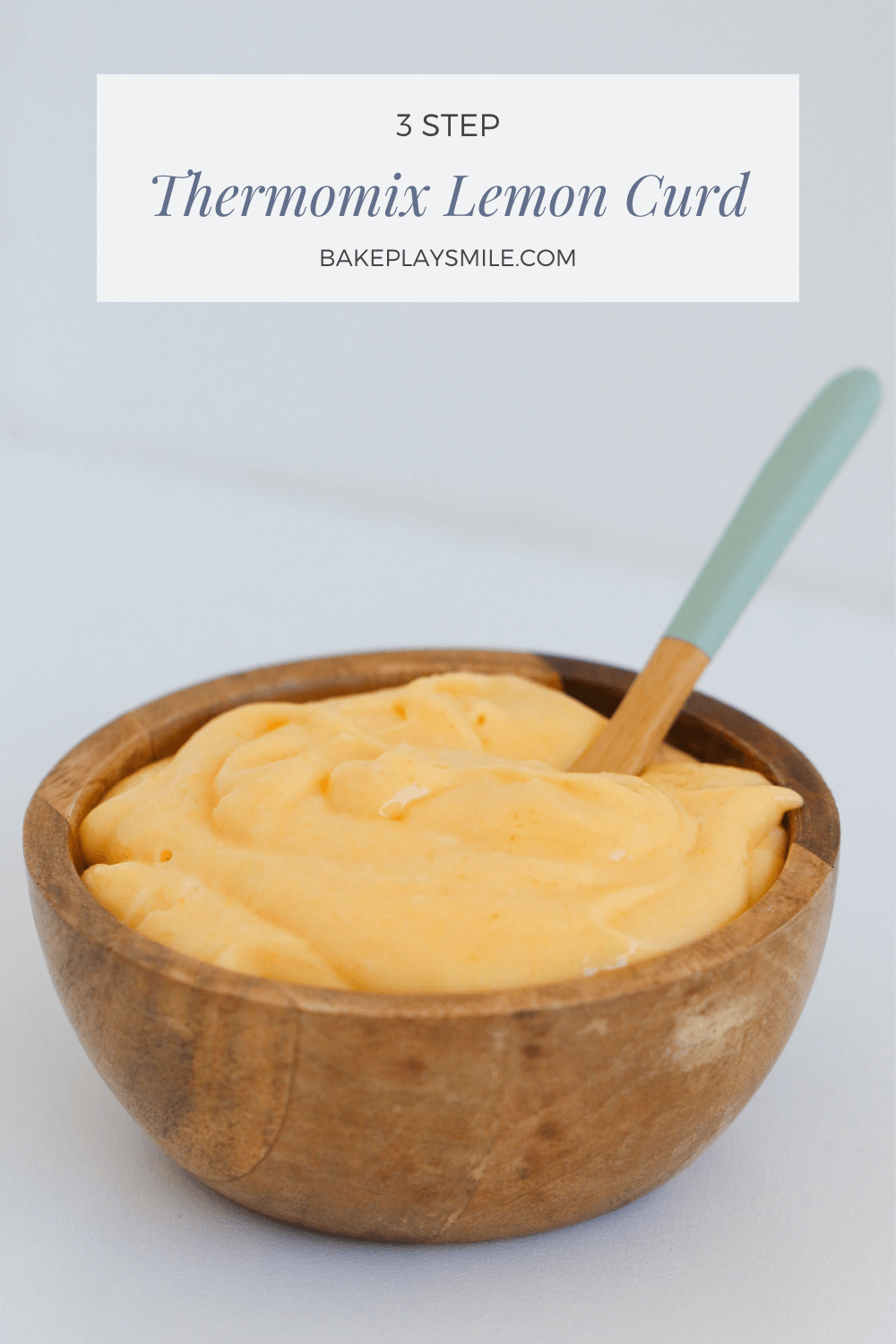 A spoon in a small wooden bowl filled with creamy yellow lemon curd.